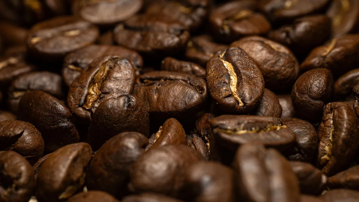 Primer plano de granos de café tostado amontonados, con la textura y el brillo del aceite bien visibles en la superficie.